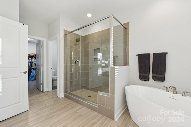 bathroom with toilet, wood-type flooring, and shower with separate bathtub