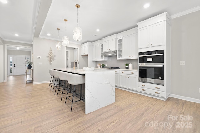 kitchen featuring sink, hanging light fixtures, a center island with sink, stainless steel double oven, and white cabinets