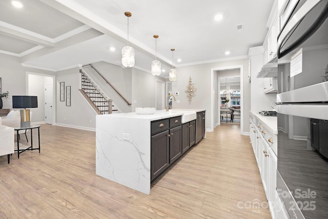 kitchen with sink, hanging light fixtures, white cabinets, a center island with sink, and light wood-type flooring