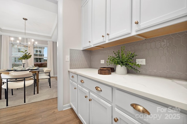 kitchen with tasteful backsplash, white cabinetry, pendant lighting, and light hardwood / wood-style floors