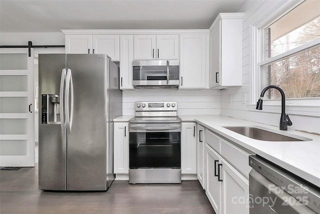 kitchen featuring a barn door, sink, stainless steel appliances, and white cabinetry