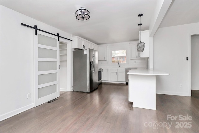 kitchen with appliances with stainless steel finishes, decorative light fixtures, white cabinetry, sink, and a barn door