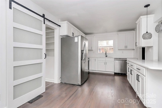 kitchen featuring a barn door, stainless steel appliances, decorative light fixtures, dark hardwood / wood-style flooring, and white cabinets