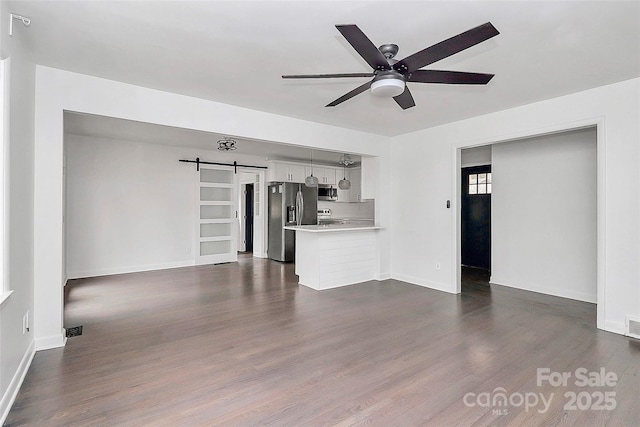 unfurnished living room featuring ceiling fan, a barn door, and dark hardwood / wood-style floors