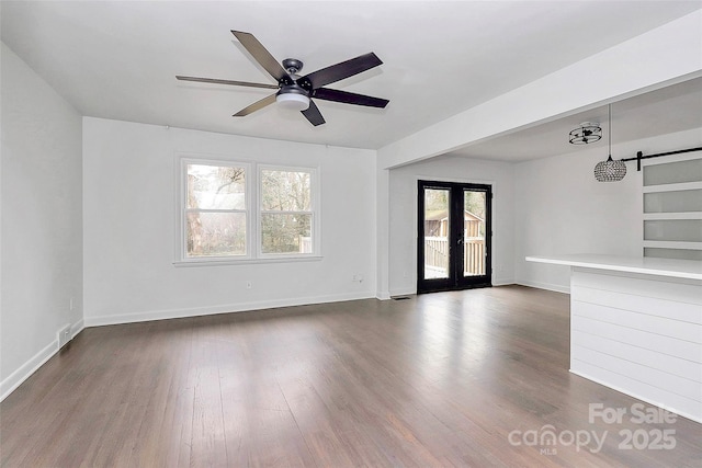 empty room featuring a healthy amount of sunlight, french doors, dark hardwood / wood-style flooring, and a barn door