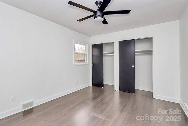 unfurnished bedroom with dark wood-type flooring, ceiling fan, and two closets