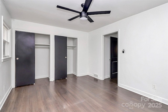 unfurnished bedroom featuring ceiling fan, dark hardwood / wood-style flooring, and multiple closets