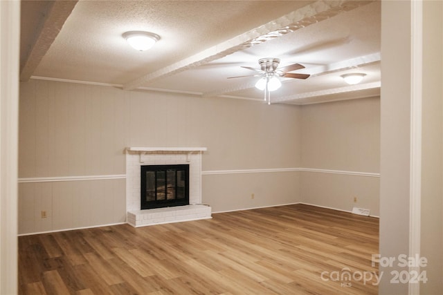 unfurnished living room featuring ceiling fan, hardwood / wood-style floors, a textured ceiling, and a brick fireplace