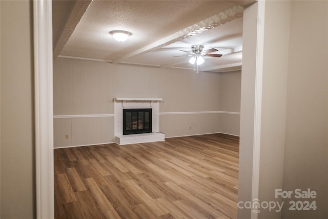 unfurnished living room with ceiling fan, hardwood / wood-style floors, a textured ceiling, and a brick fireplace