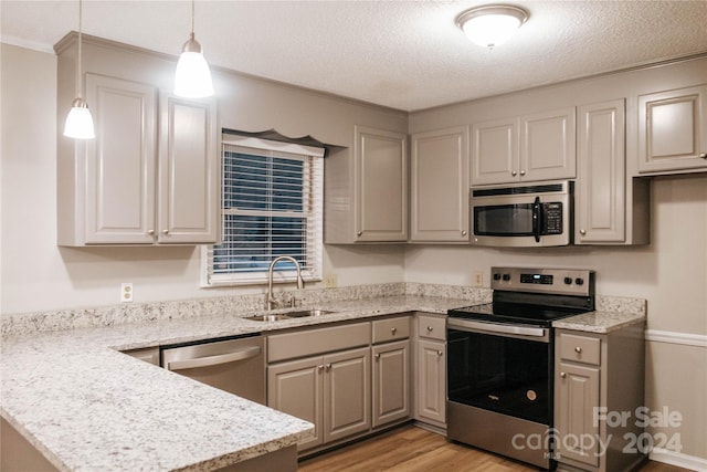 kitchen featuring appliances with stainless steel finishes, light stone counters, sink, light hardwood / wood-style floors, and hanging light fixtures