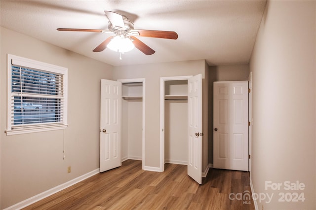 unfurnished bedroom with ceiling fan, multiple closets, a textured ceiling, and light hardwood / wood-style flooring