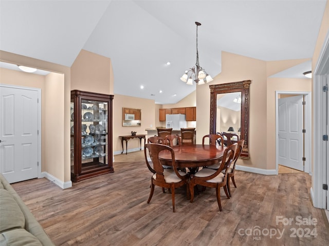 dining area with an inviting chandelier, vaulted ceiling, and light hardwood / wood-style flooring