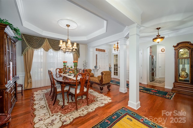 dining area featuring a notable chandelier, a raised ceiling, hardwood / wood-style floors, and ornate columns