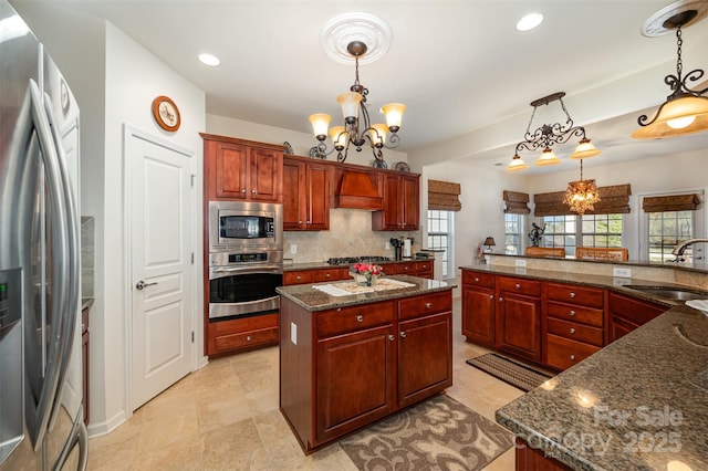 kitchen with pendant lighting, sink, appliances with stainless steel finishes, an inviting chandelier, and a center island