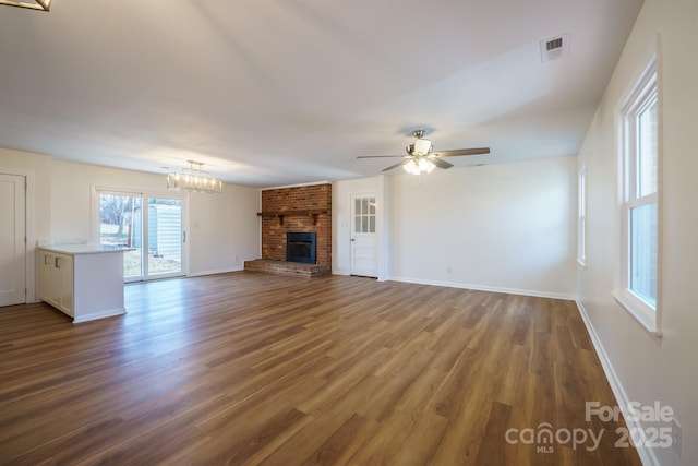 unfurnished living room featuring dark hardwood / wood-style floors, ceiling fan with notable chandelier, and a brick fireplace