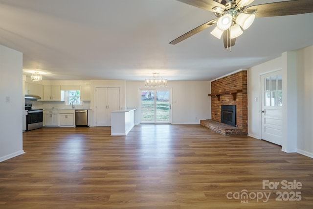 unfurnished living room featuring sink, dark wood-type flooring, ceiling fan with notable chandelier, and a brick fireplace