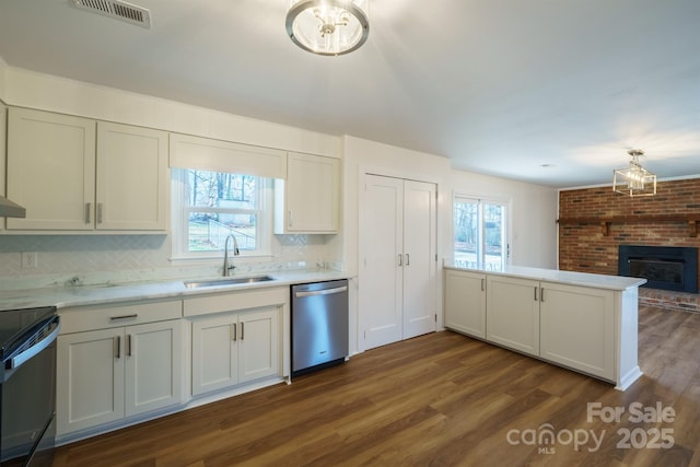 kitchen featuring stainless steel dishwasher, tasteful backsplash, sink, and a brick fireplace