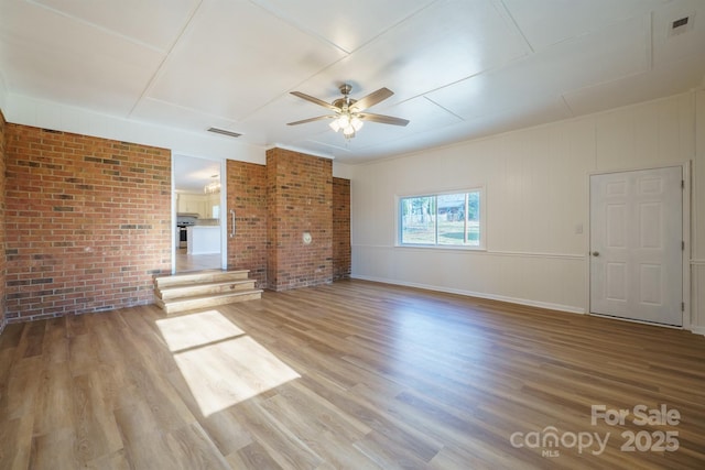 spare room featuring wood-type flooring, ceiling fan, and brick wall