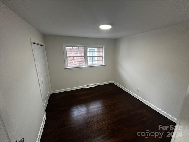 unfurnished bedroom with dark hardwood / wood-style floors, a closet, and a baseboard heating unit