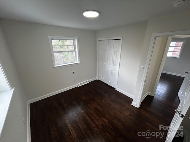 unfurnished bedroom with a closet, baseboard heating, dark wood-type flooring, and multiple windows