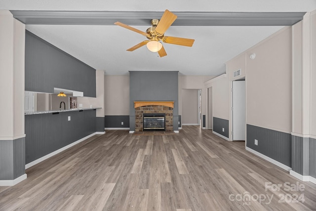 unfurnished living room with wood-type flooring, a stone fireplace, ceiling fan, and sink