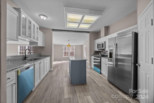 kitchen with dark stone counters, a kitchen island, appliances with stainless steel finishes, light hardwood / wood-style floors, and white cabinetry