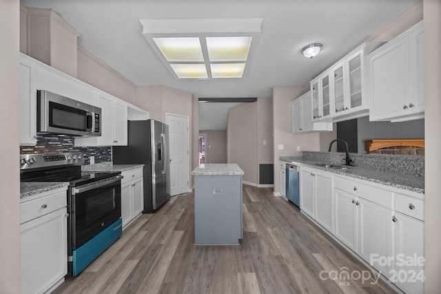 kitchen with white cabinets, appliances with stainless steel finishes, light stone counters, and hardwood / wood-style floors