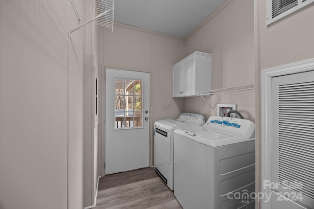 clothes washing area featuring cabinets, light wood-type flooring, a textured ceiling, crown molding, and washing machine and clothes dryer