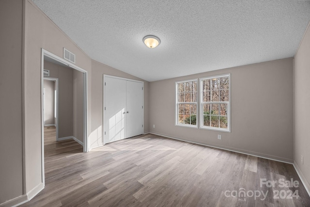 unfurnished bedroom featuring lofted ceiling, light wood-type flooring, and a textured ceiling