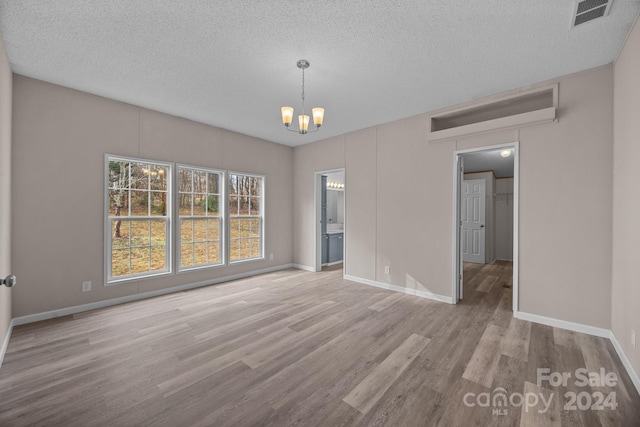 spare room featuring a textured ceiling, a notable chandelier, and light wood-type flooring