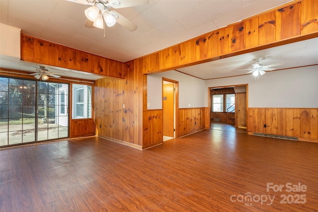 empty room with wood finished floors, baseboard heating, and ceiling fan