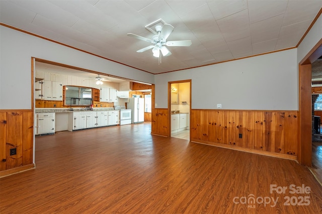 unfurnished living room with ornamental molding, wood finished floors, a ceiling fan, and a wainscoted wall