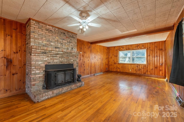 unfurnished living room with wood walls, a ceiling fan, wood finished floors, and baseboards