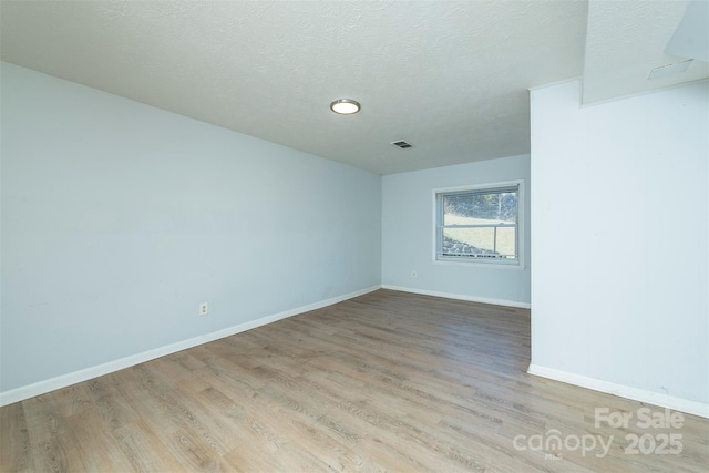 spare room featuring visible vents, light wood-type flooring, a textured ceiling, and baseboards