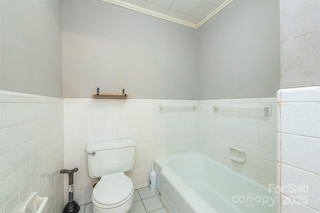 bathroom with a bath, tile patterned flooring, toilet, a wainscoted wall, and tile walls