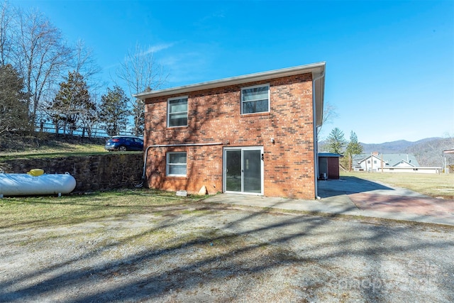 rear view of property with a mountain view, brick siding, a lawn, and a patio area