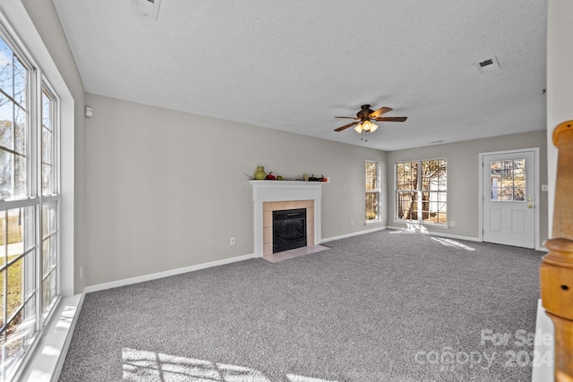 unfurnished living room with carpet flooring, a tiled fireplace, ceiling fan, and a textured ceiling