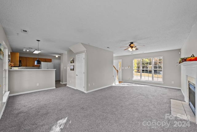 unfurnished living room featuring carpet flooring, ceiling fan, a textured ceiling, and a tiled fireplace