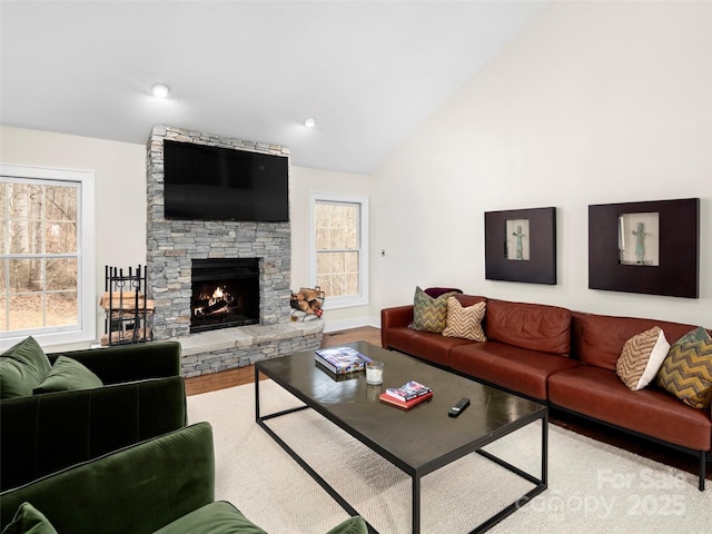 living area with lofted ceiling, a stone fireplace, plenty of natural light, and wood finished floors