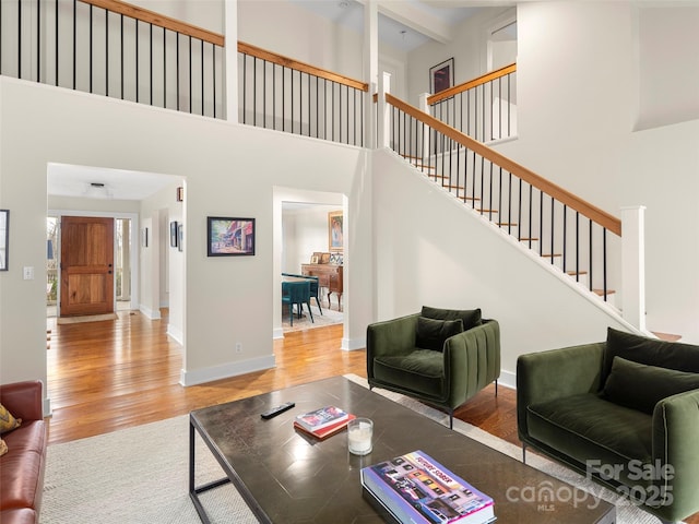 living area with a towering ceiling, stairway, baseboards, and wood finished floors