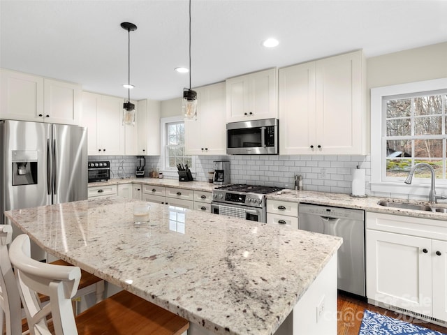 kitchen with a kitchen island, a kitchen breakfast bar, a sink, stainless steel appliances, and backsplash