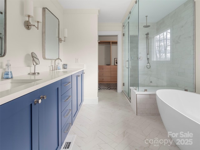 bathroom with a walk in closet, double vanity, a stall shower, a sink, and a freestanding tub