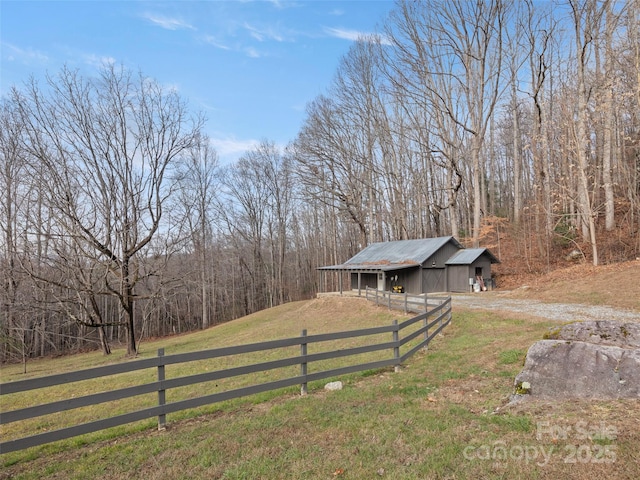 view of yard featuring driveway, a view of trees, an outbuilding, fence, and a pole building