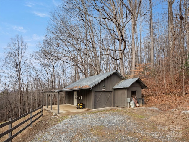 view of side of home featuring a garage, an outdoor structure, dirt driveway, and fence