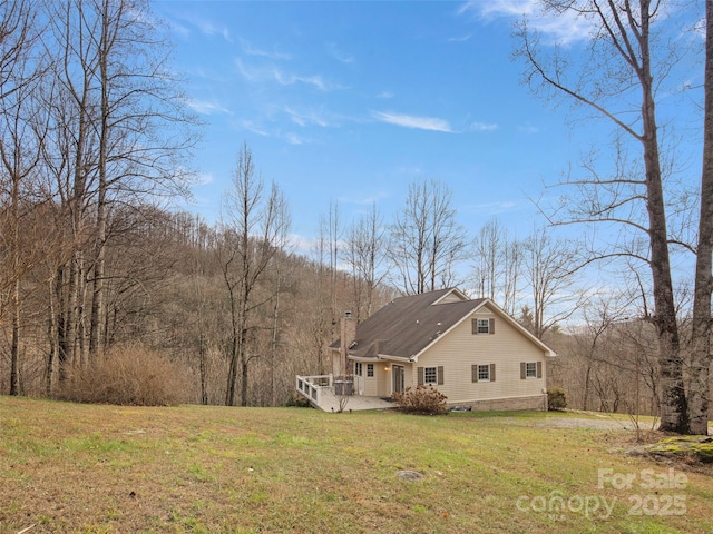 view of home's exterior featuring a forest view, a chimney, a deck, and a lawn