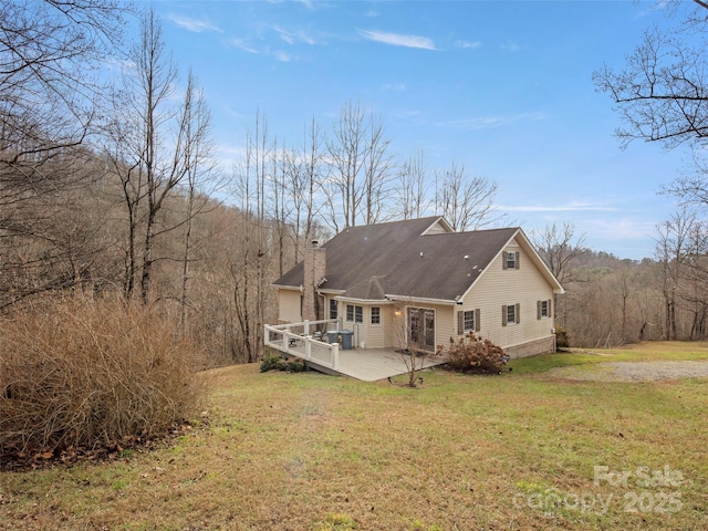 rear view of house with a deck, a yard, a chimney, and a wooded view