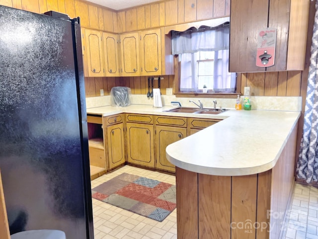 kitchen featuring wood walls, black refrigerator, kitchen peninsula, and sink