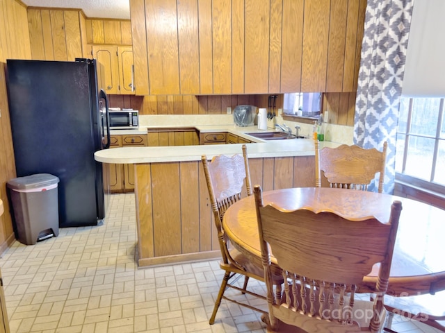 kitchen with kitchen peninsula, black fridge, sink, and wood walls