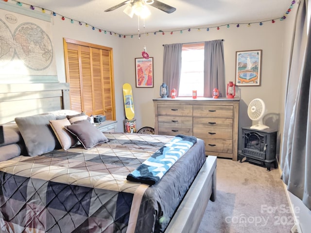 carpeted bedroom featuring ceiling fan, a wood stove, and a closet