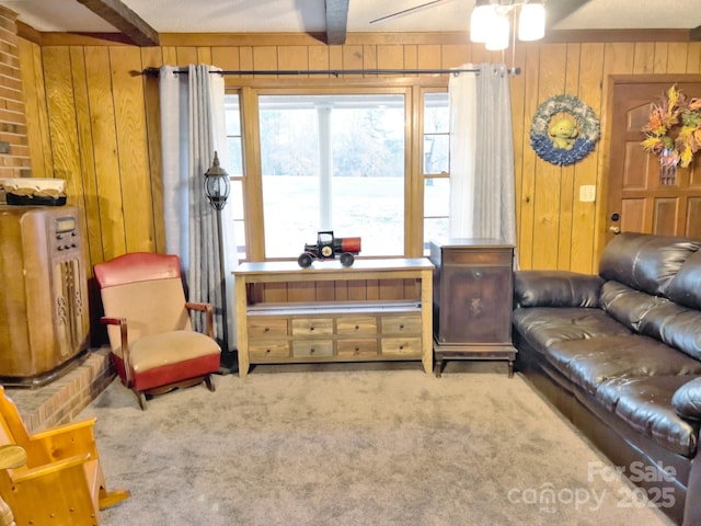 carpeted living room featuring wooden walls, beamed ceiling, and ceiling fan